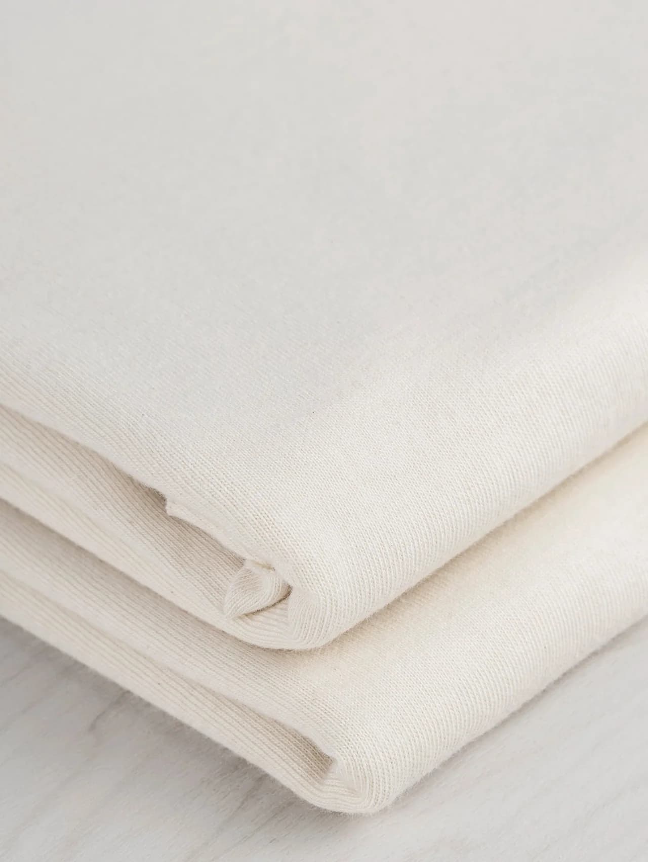 Folded natural-colour jersey showing the knitted surface and fabric edges.