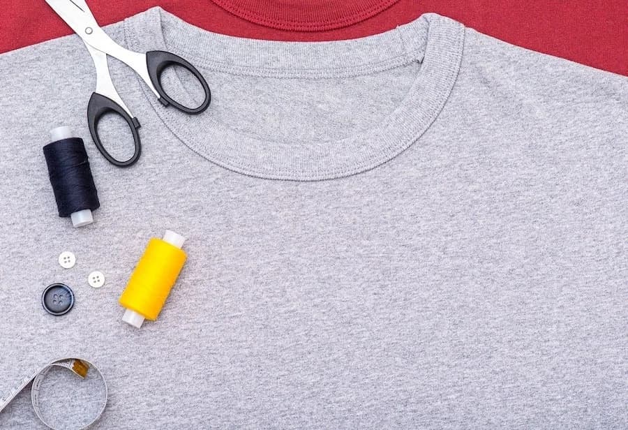 Grey crewneck T-shirt with scissors, thread and measuring tape.