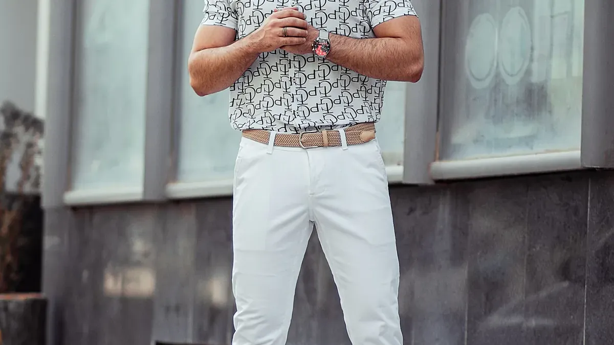 Man in white pants and blue and white checkered button up shirt standing on gray concrete