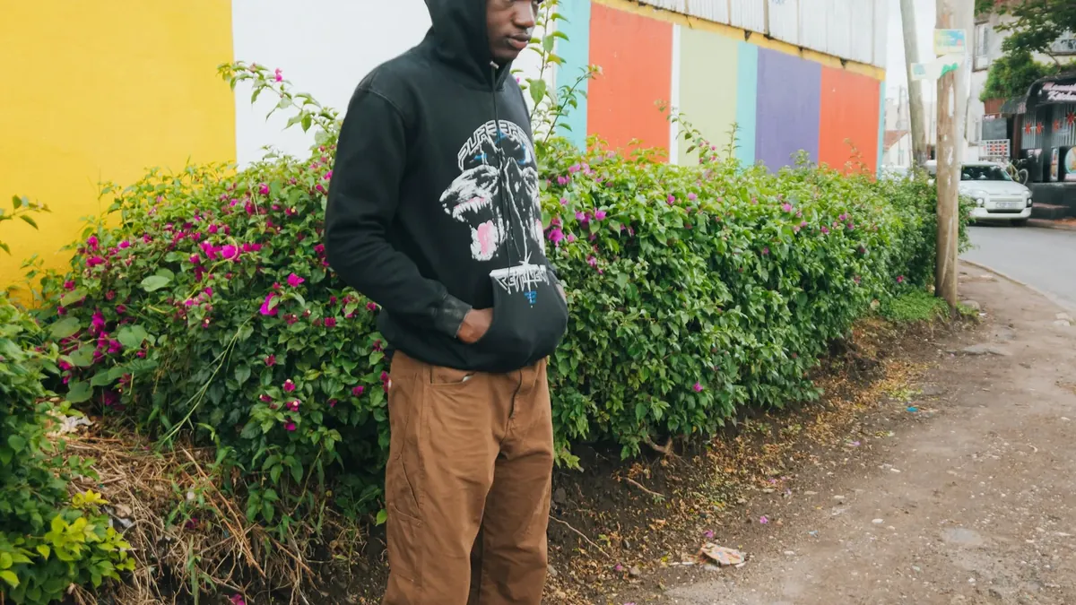 Young man in hoodie and pants stands outdoors