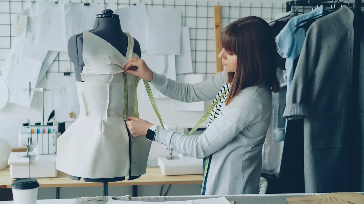 A fashion designer measures a garment on a mannequin