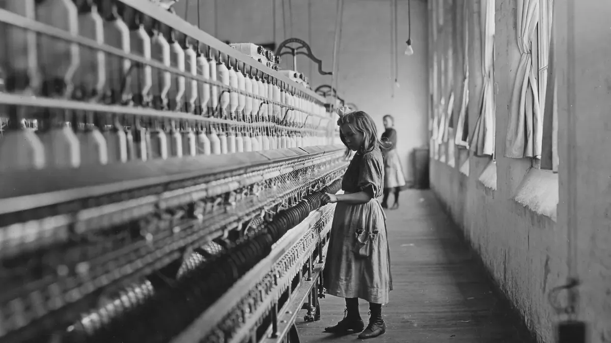A black and white photo of a woman standing in front of a loom of