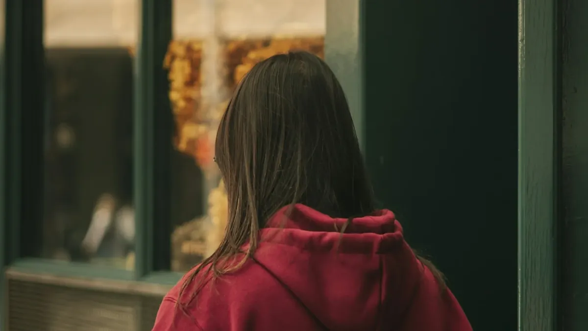 A woman in a red hoodie looking out a window