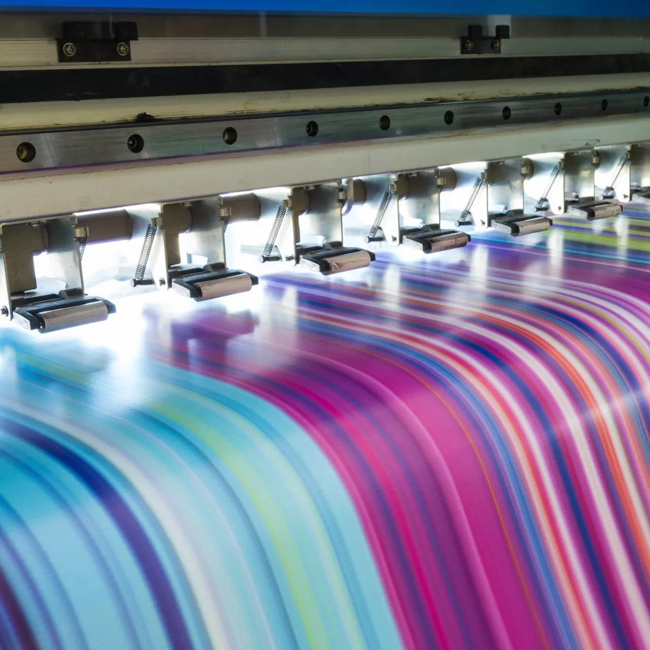 A digital textile printhead laying bands of colour onto fabric moving through the machine.
