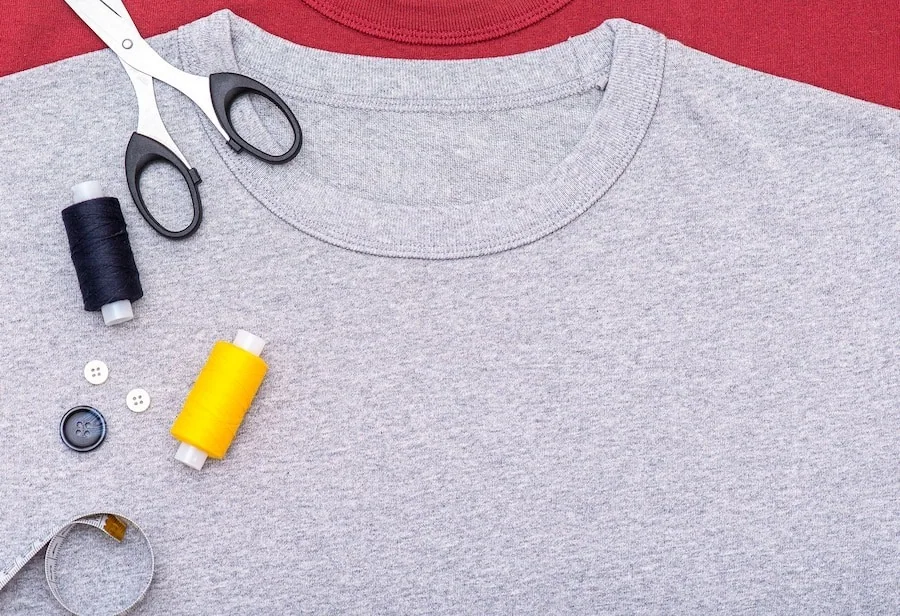 A grey crewneck T-shirt with sewing scissors, thread and measuring tape.