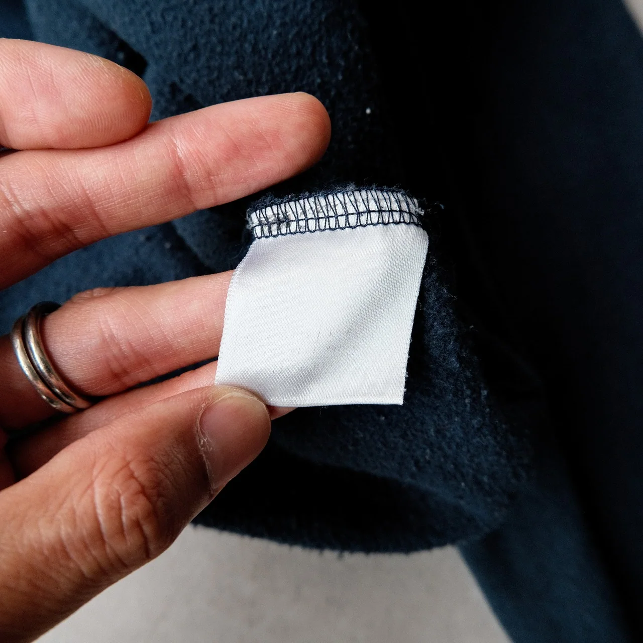 A hand showing the blank reverse of a sewn-in fabric label against dark knit material.