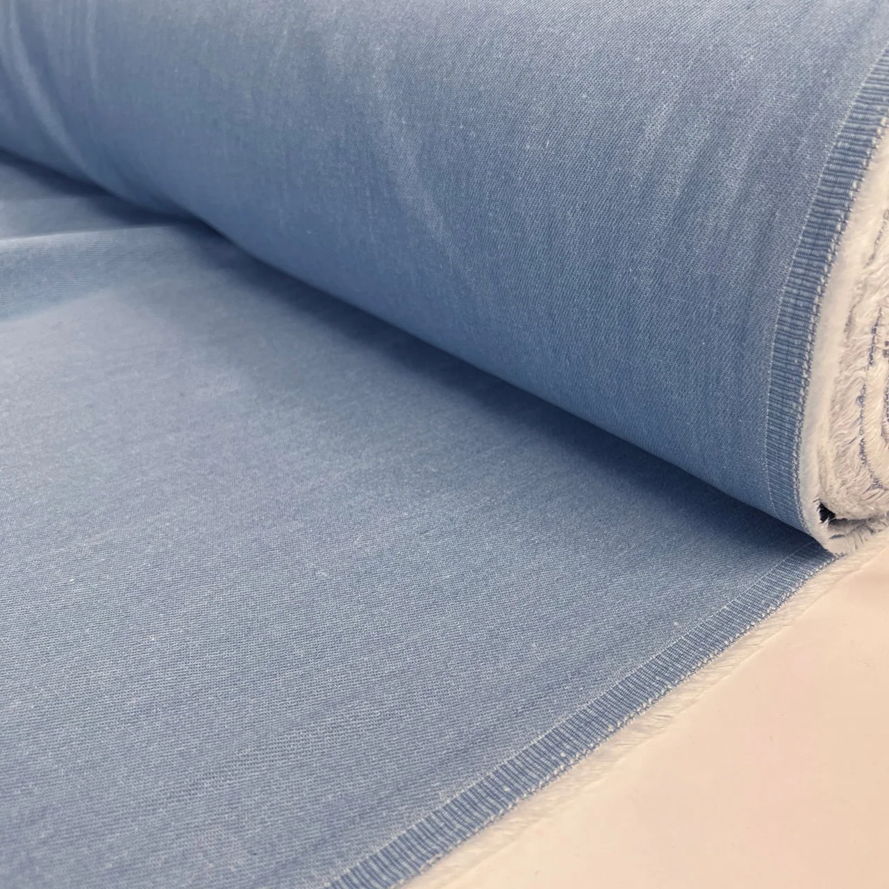 A roll of pale blue denim unrolled on a clean work surface.