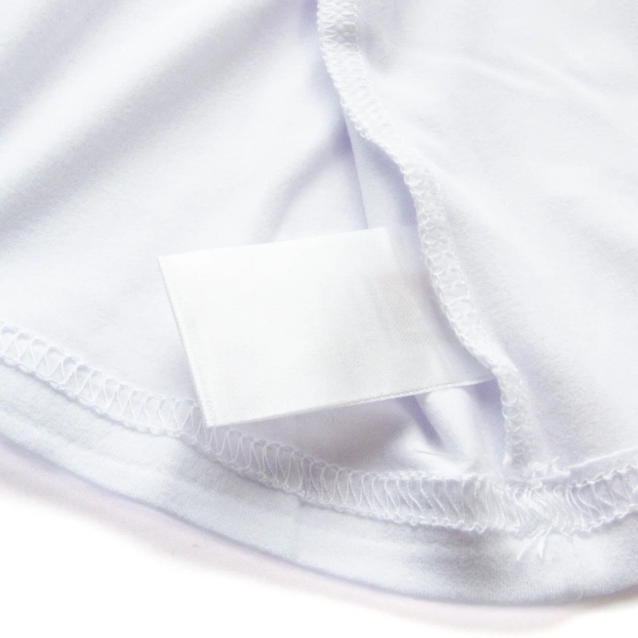 An unprinted white label sewn into a white garment seam with the overlock finish visible.
