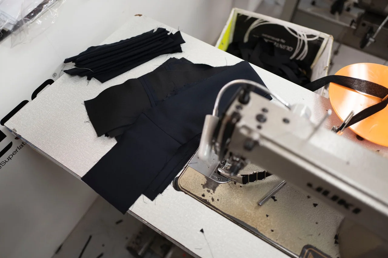 Dark garment panels and a waistband beside an industrial sewing machine.