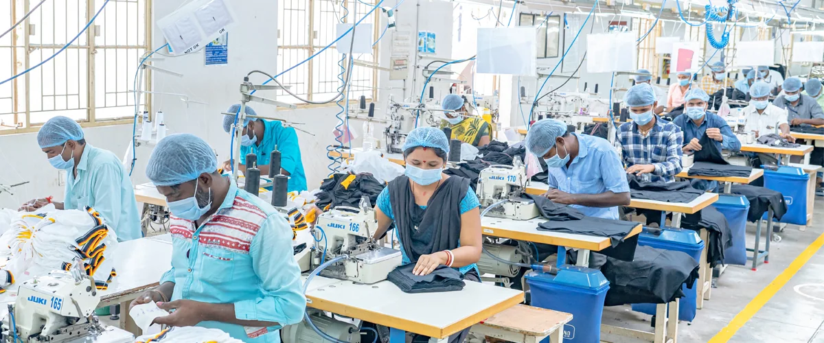 Garment workers operating rows of industrial sewing machines on a production floor.