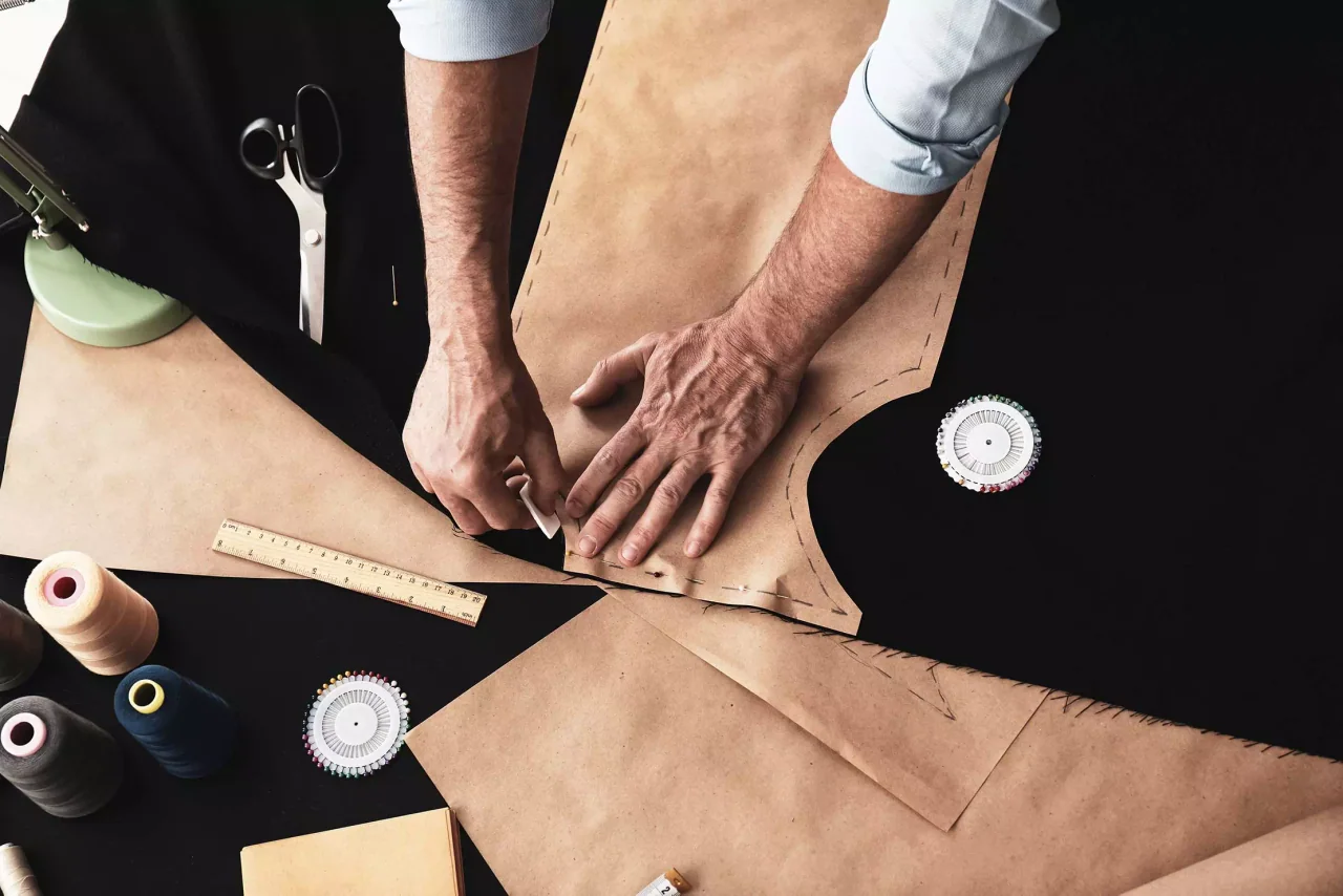 Des mains tracent un patron en papier sur un tissu foncé.