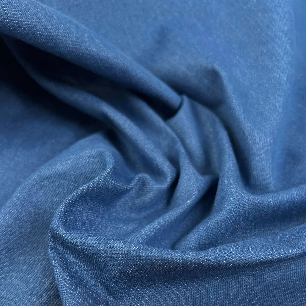 Light indigo denim draped in folds that reveal its surface texture.