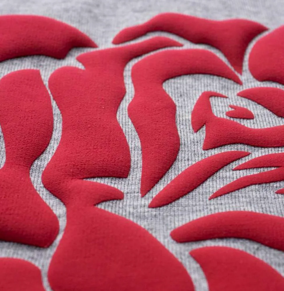 Raised red puff ink forming a floral motif on grey knit fabric, showing the print's dimensional surface.