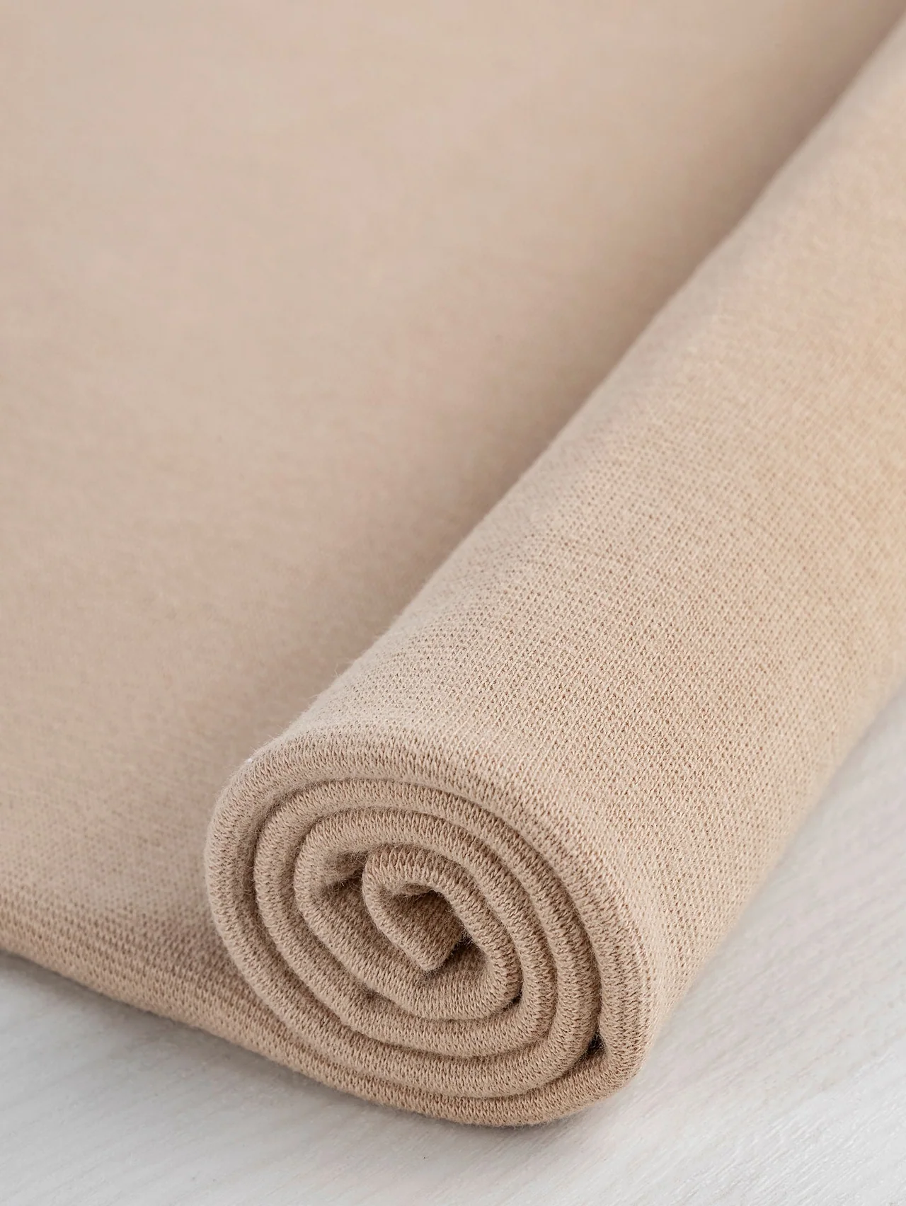 Sand-coloured rib knit folded into a roll to show the knitted surface.