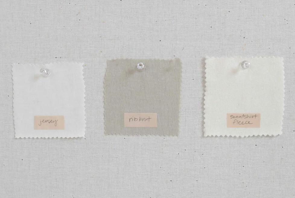 Tres muestras de tejido sujetas con alfileres que comparan punto jersey, punto acanalado y felpa perchada sobre un fondo claro.