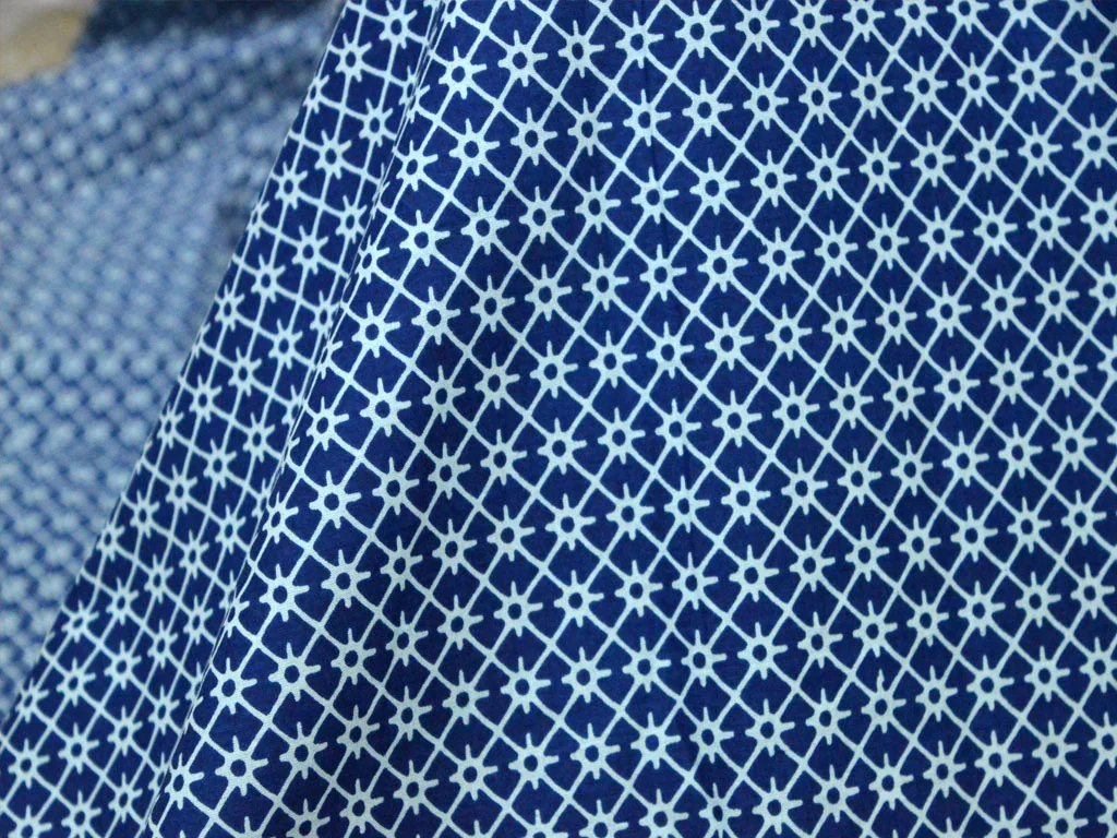 White geometric motifs repeating across blue printed cotton with the woven texture visible.