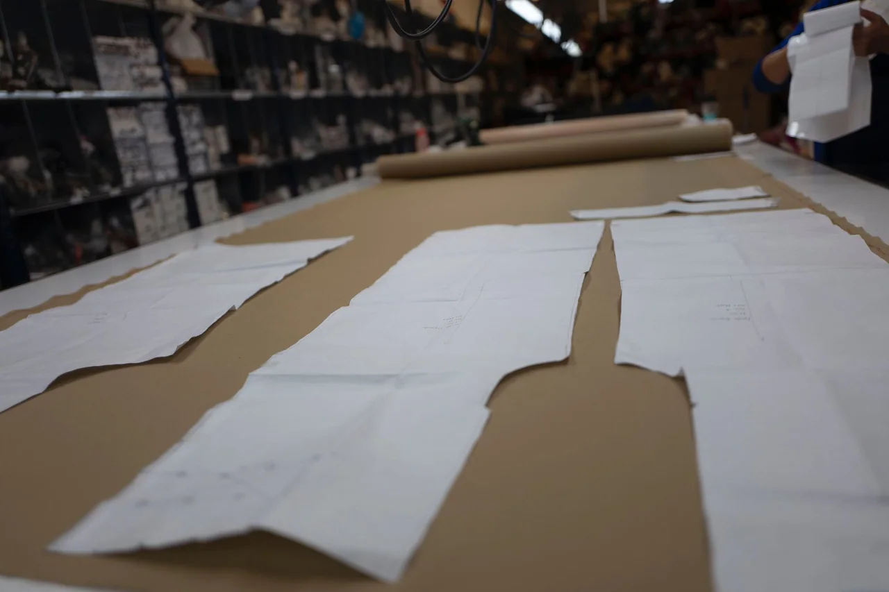 White trouser pattern pieces laid out along a long brown cutting table.
