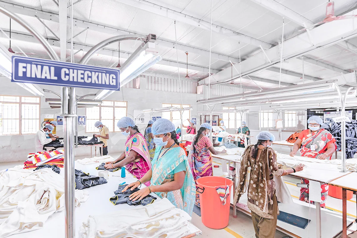 Workers reviewing garments across the final checking area of a factory.